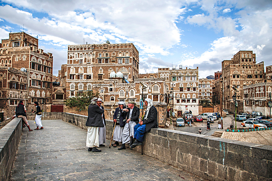 Iemenitas conversam numa ponte com edifícios históricos no fundo, na parte antiga da capital Sanaa em 15 de fevereiro de 2017. (Mohammed Huwais/AFP/Getty Images)