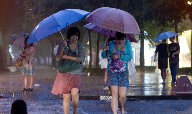 Duas chinesas atravessam uma rua alagada durante fortes chuvas em Pequim (Ed Jones/AFP/Getty Images)