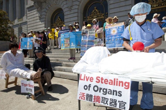 Diante da prefeitura de São Francisco, em 5 setembro de 2013, atores encenam a colheita forçada de órgãos e tortura que têm ocorrido em larga escala com praticantes do Falun Gong na China, enquanto manifestantes exibem cartazes numa conferência de imprensa para apoiar a Resolução 281 da Câmara dos EUA contra a colheita forçada de órgãos na China (Epoch Times)