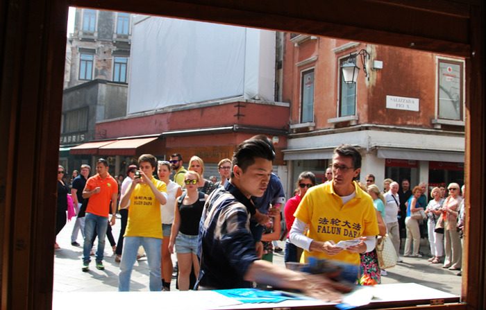 Um chinês, com um bebê nos braços, joga folhetos do Falun Gong no chão em Veneza, Itália, em 22 de setembro de 2014 (Marius Iacob)