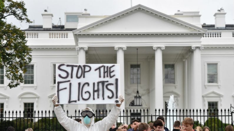 Jovem de Annapolis, Maryland, vestido com roupas de proteção e máscara, segura cartaz pedindo que não permitam mais a chegada de voos a partir de África Ocidental, num protesto em frente à Casa Branca, em Washington, DC, em 16 de outubro de 2014 (Mladen Antonov/AFP/Getty Images)