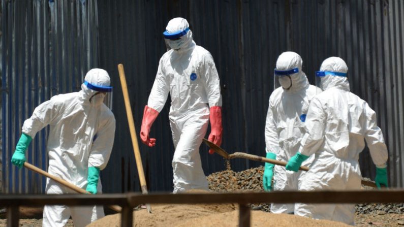 Agentes de saúde da Cruz Vermelha liberiana usam equipamentos de proteção e despejam pás de areia para absorver os fluidos emitidos a partir de corpos de vítimas do ebola em frente ao centro de gestão do ebola em Monróvia em 23 de outubro de 2014 (Zoom Dosso/AFP/Getty Images)