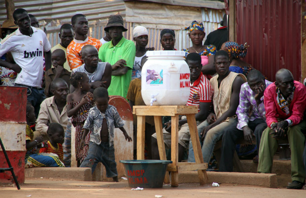 Pessoas sentam-se perto de um recipiente para lavar as mãos, na aldeia de Kouremale perto da fronteira com a Guiné, em 17 de novembro de 2014. Mali está lutando para evitar que um surto pequeno se transforme em uma grande crise após a morte de um imã guineense e de uma enfermeira do Mali que o tratou na capital Bamako (Habibou Kouyaté/AFP/Getty Images)