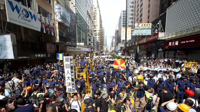 Enquanto a polícia limpa o local de protesto em Mong Kok, um manifestante de camiseta branca segura um cartaz em 26 de novembro de 2014, exigindo que as autoridades retrocedam a decisão do Congresso Popular Nacional da China sobre o sufrágio universal em Hong Kong (C.S. Poon/Epoch Times)