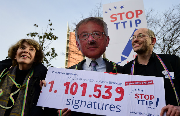 Ativista usa máscara do presidente da Comissão Europeia Jean-Claude Juncker e colegas ativistas protestam contra a Transatlantic Trade and Investment Partnership EUA-UE (TTIP), ou Acordo de Livre Comércio Transatlântico (TAFTA), no aniversário de Juncker, em frente à Comissão Europeia em Bruxelas, em 9 de dezembro de 2014 (EMMANUEL DUNAND/AFP/Getty Images)