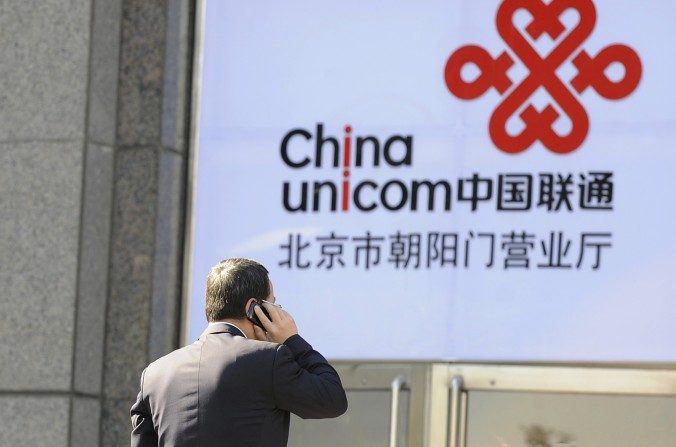 Um trabalhador fala num celular em frente de um logotipo da China Unicom, um parceiro da Apple na China, em Pequim, em 5 de janeiro de 2012. A agência anticorrupção do regime chinês publicou recentemente um relatório sobre a corrupção generalizada na terceira maior empresa mundial de telecomunicações (Liu Jin/AFP/Getty Images)