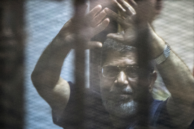 O presidente deposto do Egito Mohamed Morsi levanta as mãos dentro da cela dos réus enquanto o juiz lê seu veredito, sentenciando-o além de mais 100 outros réus à morte, na academia de polícia no Cairo em 16 de maio de 2015 (KHALED DESOUKI/AFP/Getty Images)