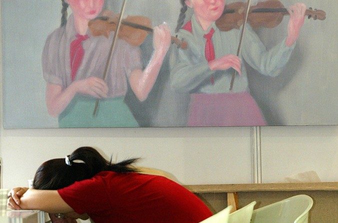 Mulher dorme diante de uma pintura de dois jovens pioneiros tocando violino no Shanghai Spring Art Salon (LIU JIN/AFP/Getty Images)