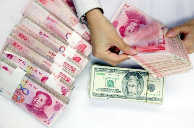 Um funcionário conta pilhas de yuans chineses e dólares norte-americanos em um banco em Xangai, China (China Photos / Getty Images)