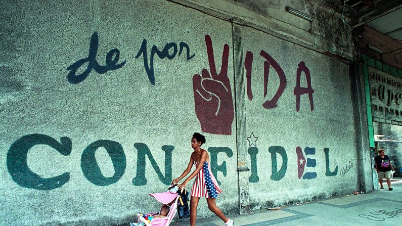 Uma mulher vestida com as cores da bandeira dos Estados Unidos empurra seu bebê enquanto passa diante de um mural que diz, "Uma vida com Fidel", em Havana, Cuba, em 11 de junho de 2001. (Jorge Rey/Getty Images)