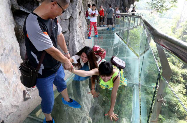 Um homem ajuda duas mulheres a atravessarem uma passarela de vidro sobre o lago Shimenxian, em Rongan, na província de Guangxi, no Sul da China. (STR/AFP/Getty Images)