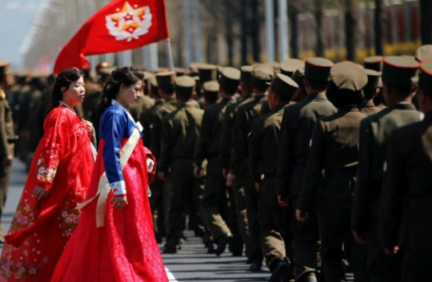 Mulheres vestidas com roupas tradicionais passam por soldados norte-coreanos em cerimônia de inauguração de um complexo residencial recém-construído na Rua Ryomyong em Pyongyang, Coreia do Norte, em 13 de abril de 2017 (Damir Sagolj/Reuters)