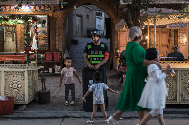 Crianças uigures brincam enquanto um policial mantem-se de prontidão em Kashgar, Xinjiang, em 29 de junho de 2017 (Kevin Frayer/Getty Images)