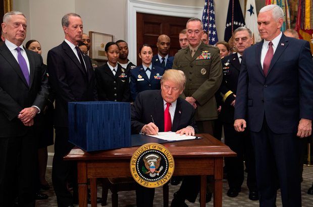 O presidente estadunidense Donald Trump, cercado por oficiais militares e membros do Congresso, incluindo o vice-presidente Mike Pence (dir.) e o secretário da defesa Jim Mattis (esq.), assina a H.R. 2810, ou Lei de Autorização da Defesa Nacional para o ano fiscal de 2018, no Salão Roosevelt na Casa Branca, em Washington, D.C., em 12 de dezembro de 2017 (Saul Loeb/AFP/Getty Images)