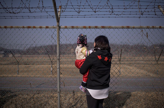 Uma mulher segura uma criança nos braços enquanto olha em direção à Coreia do Norte diante de uma cerca militar no Parque Imjingak, ao sul da Linha de Demarcação Militar e da Zona Desmilitarizada (DMZ) que separa a Coreia do Norte e a Coreia do Sul, em 19 de fevereiro de 2015. As famílias coreanas foram separadas durante a Guerra da Coreia frequentemente visitam a DMZ para oferecer orações a seus parentes no Norte durante o Ano Novo Lunar (Ed Jones/AFP/Getty Images)