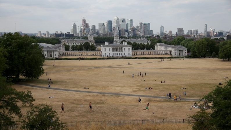 Prédios de instituições financeiras, incluindo JPMorgan Chase, Citi, HSBC, e outras do distrito comercial Canary Wharf, aparecem no horizonte enquanto visitantes do Greenwich Park caminham e brincam na grama seca ao leste de Londres em 23 de julho de 2018 (Daniel Leal-Olivas/AFP/Getty Images)