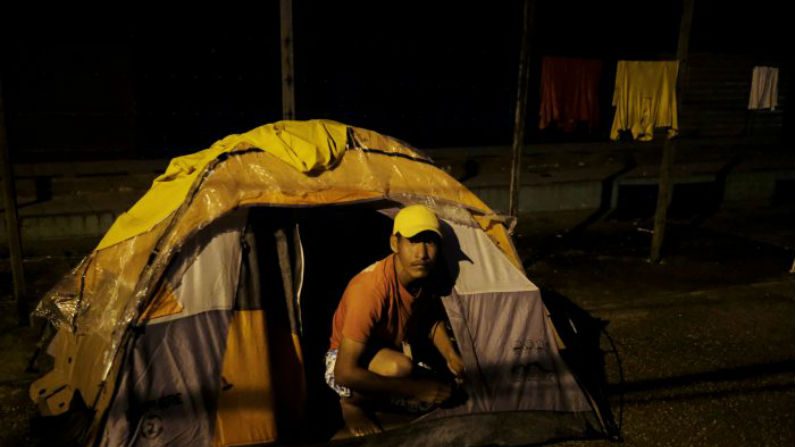 Homem venezuelano é retratado na entrada de sua tenda, montada ao longo da rua, enquanto espera para mostrar seu passaporte ou bilhete de identidade no dia seguinte no controle de fronteira de Pacaraima, estado de Roraima, em 8 de agosto de 2018 (Nacho Doce / REUTERS)