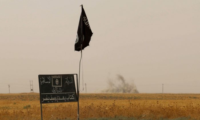 Fumaça sobe à distância atrás de uma bandeira do ISIS depois que combatentes iraquianos curdos Peshmerga teriam capturado várias aldeias do Estado Islâmico no distrito de Daquq, no Iraque, em 11 de setembro de 2015 (Marwan Ibrahim / AFP / Getty Images)