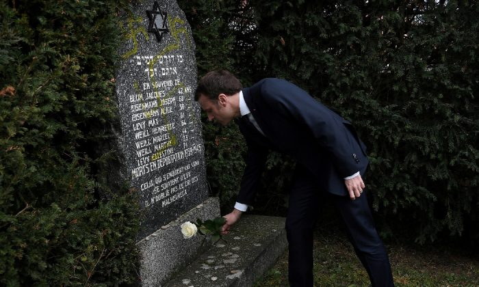 O presidente francês Emmanuel Macron coloca uma rosa branca em um túmulo vandalizado com suásticas durante uma visita ao cemitério judaico em Quatzenheim, França, em 19 de fevereiro de 2019 (Frederick Florin / Pool via Reuters)