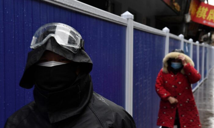 Pessoas usam máscaras enquanto caminham ao lado de barreiras estabelecidas em uma área residencial em Wuhan, o epicentro do novo surto de coronavírus na província de Hubei, na China, em 28 de fevereiro de 2020 (Stringer / Reuters)