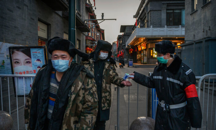 Um homem chinês usa uma máscara protetora enquanto ele e outros têm sua temperatura verificada por um guarda em uma entrada temporária em uma área comercial em Pequim, em 11 de março de 2020 (Kevin Frayer / Getty Images)