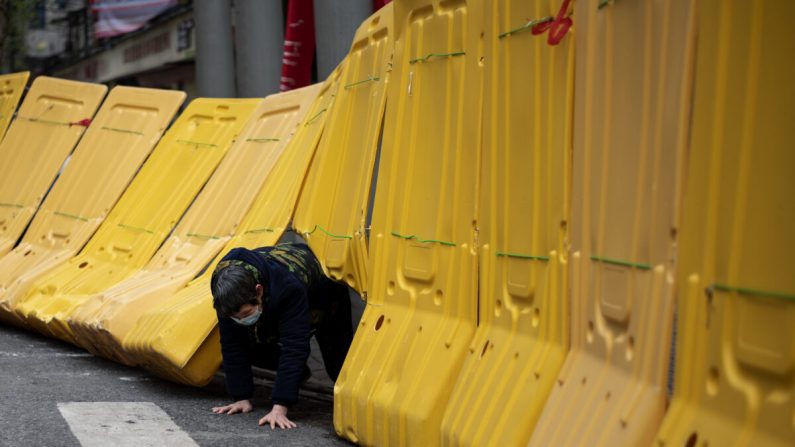 Uma mulher idosa rasteja sob uma barricada amarela que separa um complexo residencial em Wuhan, China, em 2 de abril de 2020 (NOEL CELIS / AFP via Getty Images)