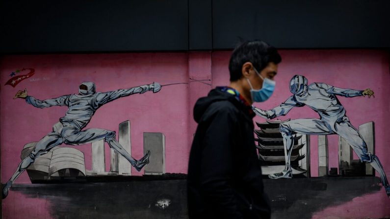 Um homem de máscara facial passa por um mural ao longo de uma rua em Wuhan, província central de Hubei, China, em 2 de abril de 2020 (NOEL CELIS / AFP via Getty Images)