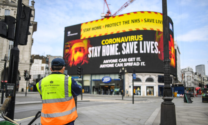 Um gari é visto em frente às mensagens do vírus do PCC no Piccadilly Circus, em Londres, em 8 de abril de 2020 (Peter Summers / Getty Images)