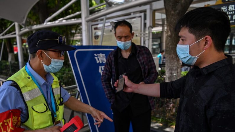 Um trabalhador digitaliza o código de saúde gerado pelo aplicativo de celular de um passageiro e também examina sua temperatura corporal antes que o passageiro possa pegar um táxi na Estação Ferroviária Hankou em Wuhan, China, em 12 de maio de 2020 (HECTOR RETAMAL / AFP via Getty Images)