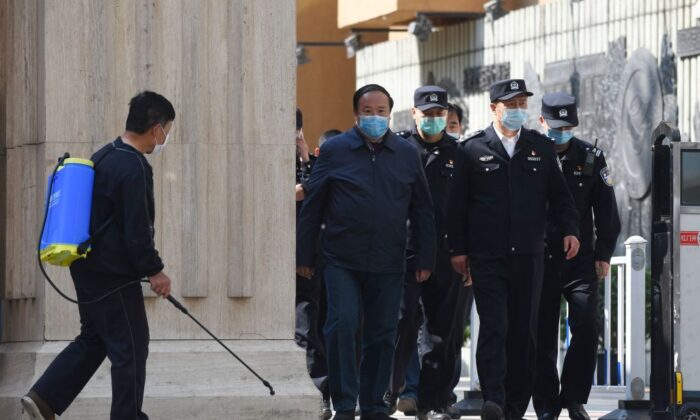 Policiais e oficiais saem de uma escola de ensino médio enquanto um homem (à esquerda) desinfeta a entrada em Pequim, em 27 de abril de 2020 (Greg Baker / AFP via Getty Images)