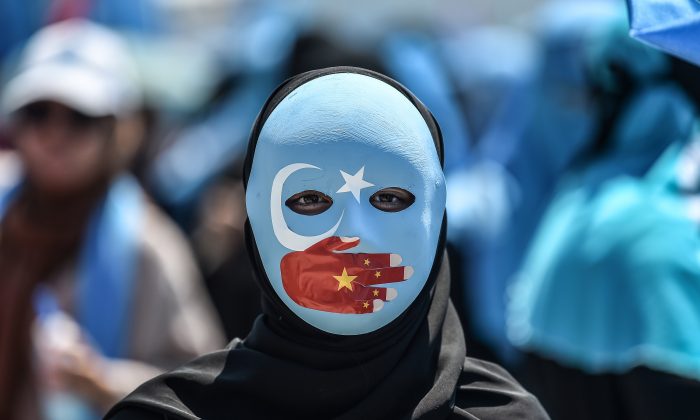 Um manifestante vestindo uma máscara pintada com as cores da bandeira do Turquestão Oriental - como alguns separatistas uigures se referem à região de Xinjiang - e uma mão com as cores da bandeira chinesa, participa de um protesto denunciando o tratamento da China aos muçulmanos uigures étnicos frente ao consulado chinês em Istambul, em 5 de julho de 2018 (OZAN KOSE / AFP / Getty Images)
