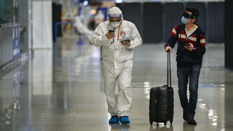 Um membro da segurança do aeroporto, usando equipamento de proteção contra o surto de coronavírus COVID-19, caminha com um passageiro na chegada ao Aeroporto Internacional de Shanghai Pudong em Xangai em 26 de março de 2020 (Foto: HECTOR RETAMAL / AFP via Getty Images)
 