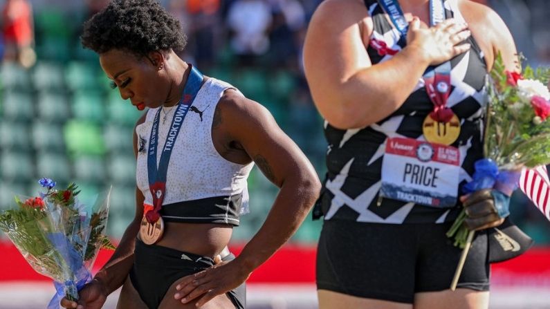 Gwendolyn Berry (E), terceira colocada, se afasta da bandeira dos EUA durante o Hino Nacional dos EUA, enquanto DeAnna Price (C.), primeira colocada, também está no pódio após a final. Lançamento do martelo feminino no dia 9 das Olimpíadas dos EUA Provas por equipes de atletismo (Patrick Smith / Getty Images)
