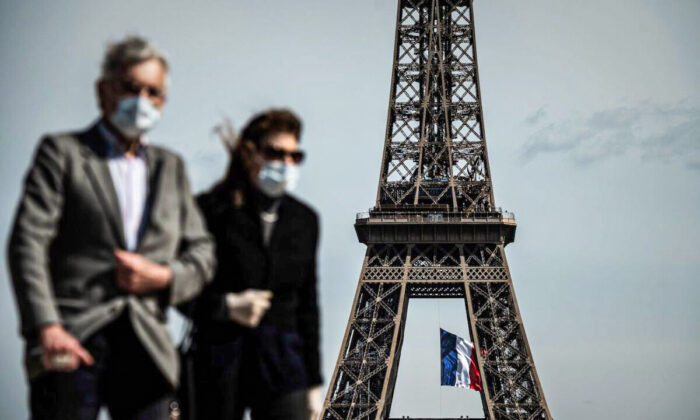 Um homem e uma mulher usando máscaras caminham na Trocadero Plaza enquanto uma bandeira nacional francesa é hasteada na Torre Eiffel ao fundo, em Paris, no dia 11 de maio de 2020 (Philippe Lopez / AFP via Getty Images)