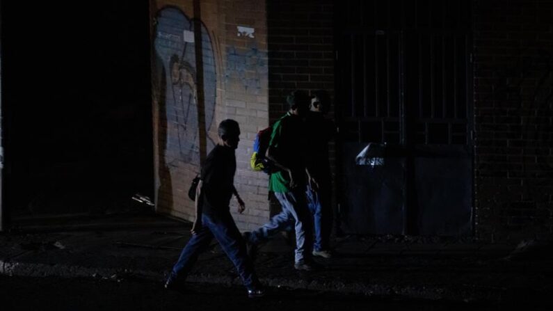 O farol de um carro ilumina um grupo de homens que caminham por uma rua durante um apagão em Caracas, na Venezuela, no dia 13 de junho de 2021 (EFE/ Rayner Pena R)
