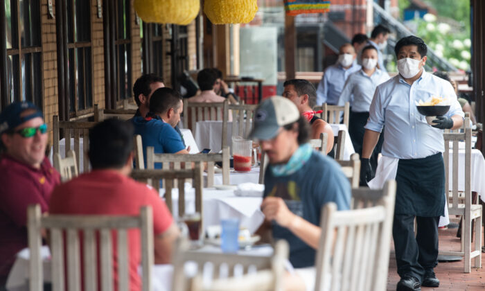 Um garçom usando máscara e luvas entrega comida em uma mesa para clientes sentados em um pátio ao ar livre em um restaurante mexicano em Washington, em 29 de maio de 2020 (Saul Loeb/AFP via Getty Images)