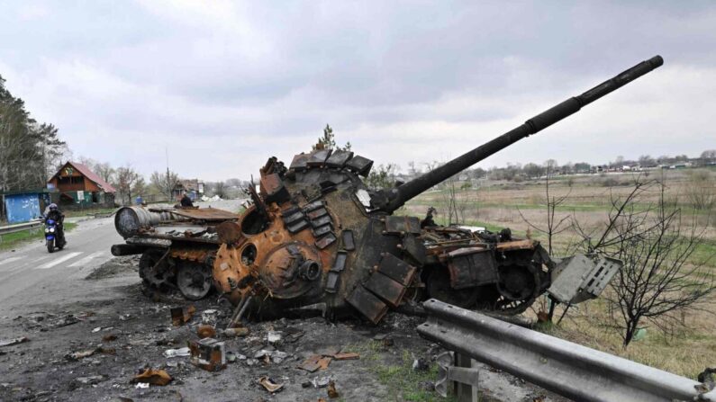 Um homem passa de moto por um tanque russo destruído em uma estrada no vilarejo de Rusaniv, perto de Kiev, na Ucrânia, em 16 de abril de 2022 (Genya Savilov/AFP/Getty Images)