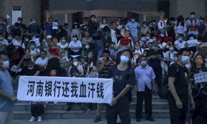 Pessoas seguram faixas e cantam slogans para protestar na entrada de uma agência do banco central da China em Zhengzhou, na província de Henan, no centro da China, em 10 de julho de 2022. Uma grande multidão de depositantes de bancos chineses furiosos enfrentou a polícia em 10 de julho , alguns supostamente feridos quando foram levados grosseiramente. Este caso chamou a atenção por causa de tentativas anteriores de usar um aplicativo de rastreamento COVID-19 para impedir que eles se mobilizassem (Yang/AP Photo)