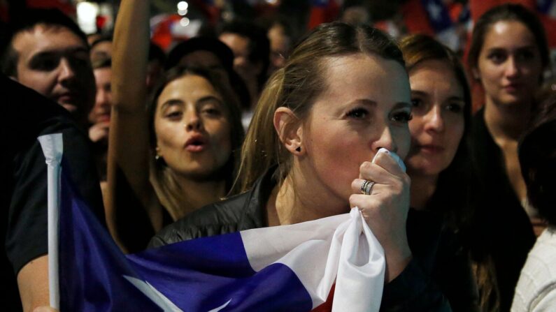 Uma mulher beija uma bandeira chilena enquanto pessoas que rejeitam o novo projeto de constituição comemoram após conhecer os primeiros resultados da votação do plebiscito, em Santiago, em 4 de setembro de 2022 (Foto de CLAUDIO REYES/AFP via Getty Images)
