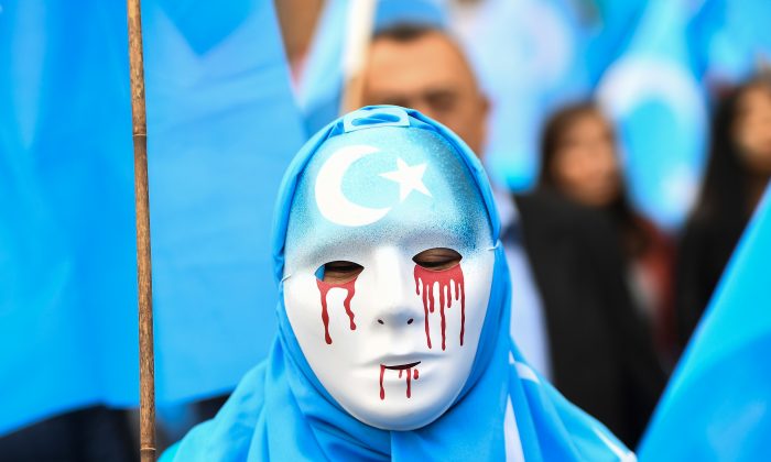 Uma pessoa usando uma máscara branca com lágrimas de sangue participa de uma marcha de protesto de uigures étnicos pedindo à União Europeia que pressione a China a respeitar os direitos humanos na região chinesa de Xinjiang e peça o fechamento do "centro de reeducação" onde Uigures são detidos, durante uma manifestação em torno das instituições da UE em Bruxelas, em 27 de abril de 2018 (Emmanuel Dunand/AFP/Getty Images)