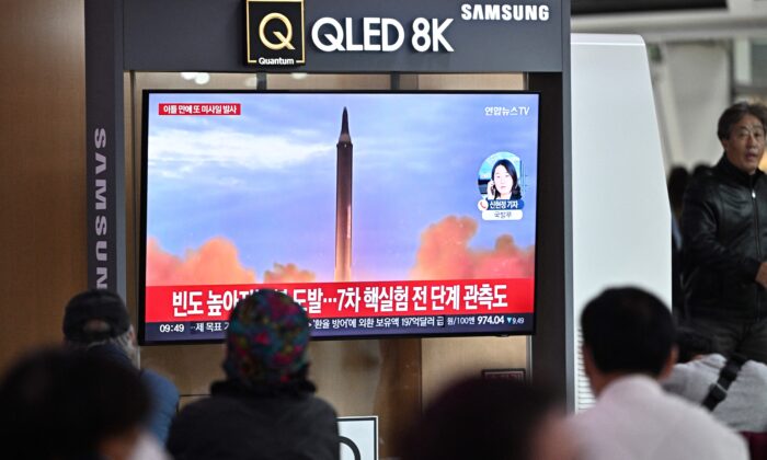 Pessoas sentadas próximo a uma televisão assistindo ao noticiário com imagens de arquivo de um teste de míssil norte-coreano, em uma estação ferroviária em Seul em 6 de outubro de 2022 (Anthony Wallace/AFP via Getty Images)