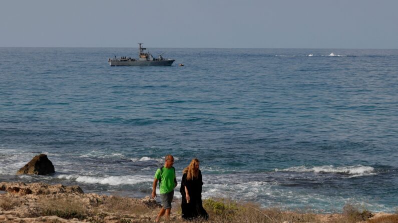 Pessoas caminham ao longo da praia enquanto um navio da marinha patrulha as águas do Mediterrâneo ao largo de Rosh Hanikra, conhecido no Líbano como Ras al-Naqura, no lado israelense da fronteira entre os dois países, em 7 de outubro de 2022 (Foto de JALAA MAREY/AFP via Getty Images)