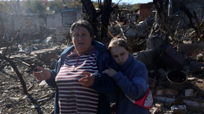 Uma menina e sua avó, moradores locais, reagem ao lado de uma casa destruída como resultado de um bombardeio na cidade de Kupiansk, região de Kharkiv, em 17 de outubro de 2022, quando a guerra Rússia-Ucrânia entra em seu 236º dia (Foto de ANATOLII STEPANOV /AFP via Getty Images)