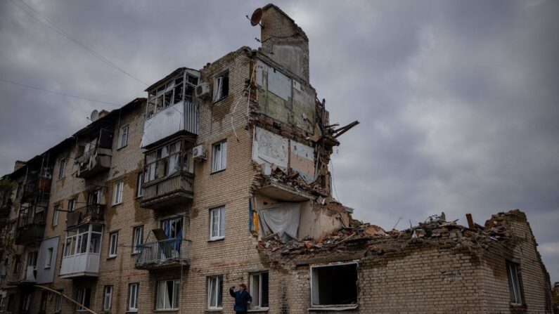 Um homem tira fotos com um telefone ao lado de um prédio danificado em Lyman, região de Donetsk, em 21 de outubro de 2022, após a recaptura da área pelas forças russas, em meio à invasão russa da Ucrânia (Foto de DIMITAR DILKOFF/AFP via Getty Imagens)