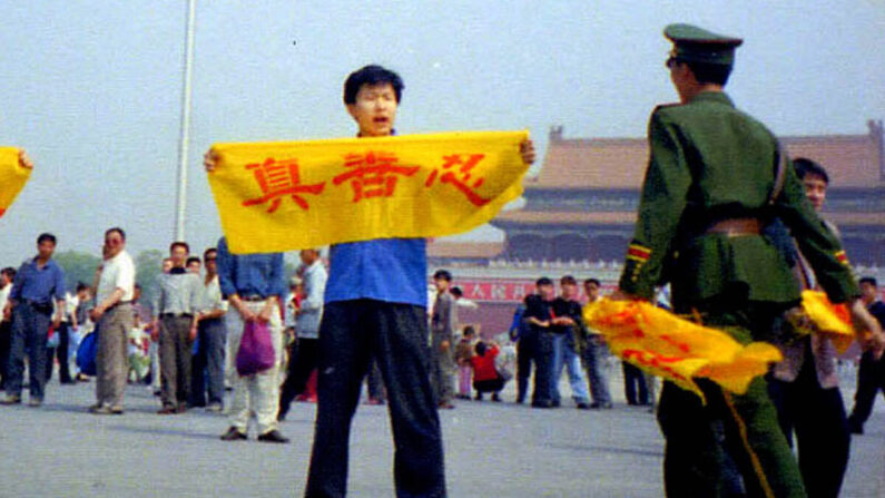 Um policial chinês se aproxima de um praticante do Falun Gong na Praça Tiananmen, em Pequim, enquanto ele segura uma faixa com os caracteres chineses para “verdade, compaixão e tolerância”, os princípios centrais do Falun Gong. (Cortesia de Minghui.org)