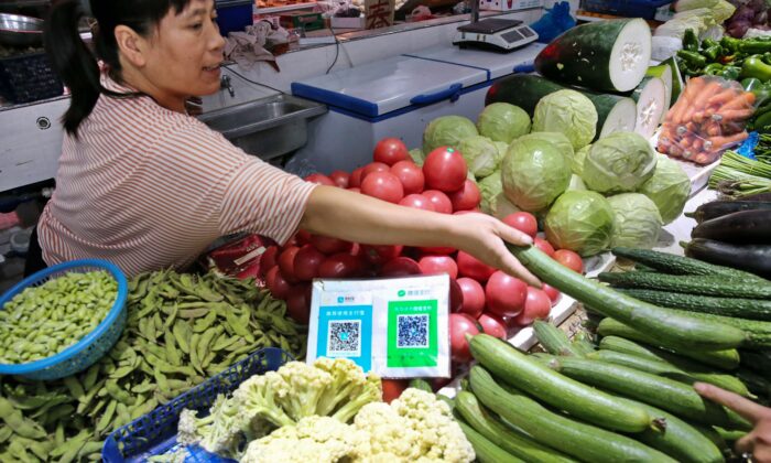 Os códigos QR do Alipay e do WeChat para pagamento online são exibidos enquanto um vendedor (L) ensaca vegetais para um cliente em um mercado na cidade de Nantong, província de Jiangsu, China, em 10 de setembro de 2018. (STR/AFP via Getty Images)