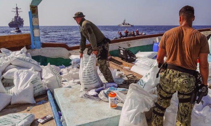 O contratorpedeiro de mísseis guiados USS The Sullivans e o navio costeiro de patrulha USS Hurricane, navegam ao fundo enquanto os marinheiros dos EUA fazem o inventário de uma grande quantidade de fertilizante de ureia e perclorato de amônio, descobertos a bordo de um navio de pesca interceptado por forças navais enquanto transitava em águas internacionais, no Golfo de Omã, em 9 de novembro de 2022. (Cortesia da Marinha dos EUA pelo técnico de sonar "Surface" 1ª classe Kevin Frus)