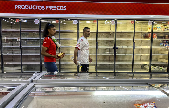 Duas pessoas caminham em frente às geladeiras quase vazias de um supermercado, em 14 de março de 2023, em Buenos Aires, Argentina (EFE / Juan Ignacio Roncoroni)