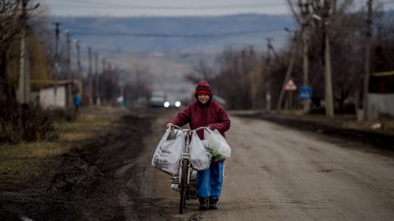 Uma mulher empurra uma bicicleta por uma rua em Konstantinovka, região de Donetsk, em 1º de março de 2023, em meio à invasão russa da Ucrânia (Foto de DIMITAR DILKOFF/AFP via Getty Images)