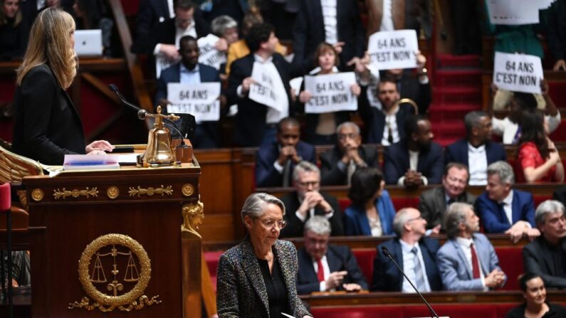 Membros do Parlamento da coalizão de esquerda NUPES (Nova União Ecológica e Social do Povo) seguram cartazes enquanto a primeira-ministra da França Elisabeth Borne (C) chega para confirmar a força através da lei previdenciária sem votação do parlamento durante uma sessão sobre a reforma previdenciária do governo na Assembleia Nacional da Câmara, em Paris, em 16 de março de 2023 (Foto de ALAIN JOCARD/AFP via Getty Images)